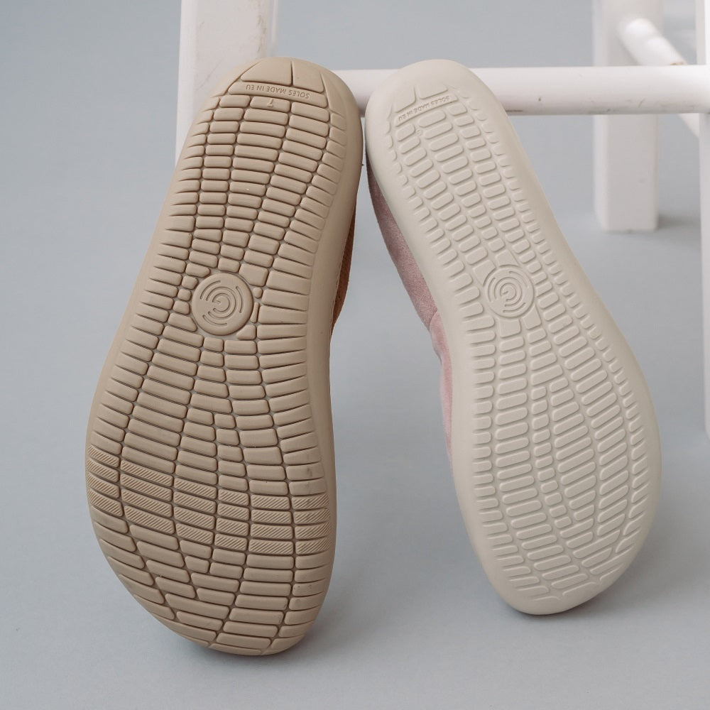 A photo of Groundies Lily Classic flats with a leather upper and tan rubber true sense soles. The flats are a perforated leather in a cognac color with trim around the tops. The interior of the flats is a light beige color. The left flat is shown from below next to a right light pink Lily Soft flat, showing the soles of both shoes. #color_cognac