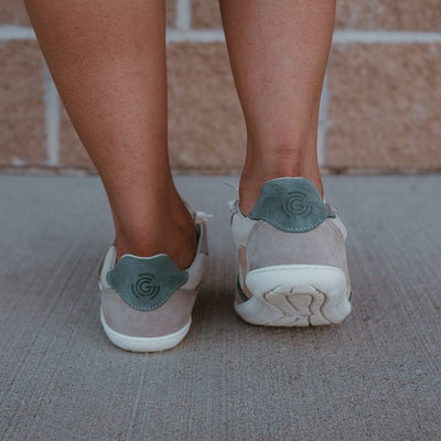 Groundies Nova GO1 leather Sneakers. Sneakers are a cream leather base with suede beige, sage green, and tan color blocks. Both shoes are shown from behind on a dark-skinned woman standing on pavement #color_beige-sage-green