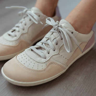 A photo of Groundies Nova GO1 Sneakers made with soft leather and white rubber soles. The sneakers have Beige, Periwinkle, and Pink color blocks. Both shoes are shown from the diagonal left against a grey floor in this photo. #color_beige-lavender-pink