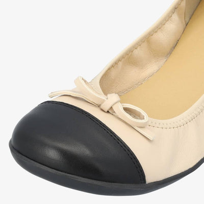 Beige & Black Groundies Ruby leather ballet flat. Shoes are light beige with a leather bow, black leather toe cap, black soles, and elastic around the openiing. Left shoe toe box is shown close up here facing diagonally to the left against a white background. #color_beige-black