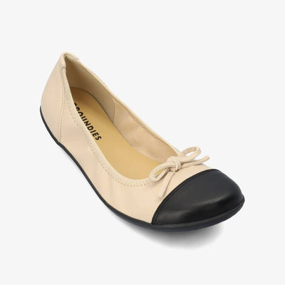 Beige & Black Groundies Ruby leather ballet flat. Shoes are light beige with a leather bow, black leather toe cap, black soles, and elastic around the openiing. Right shoe is shown here diagonally to the right against a white background. #color_beige-black