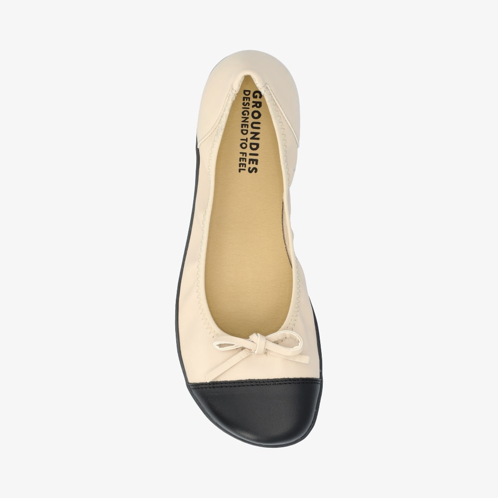 Beige & Black Groundies Ruby leather ballet flat. Shoes are light beige with a leather bow, black leather toe cap, black soles, and elastic around the openiing. Right shoe is shown here from above against a white background. #color_beige-black