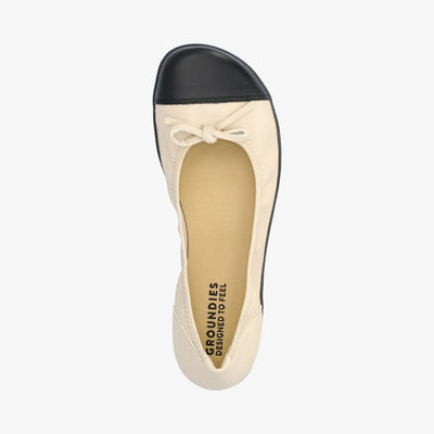 Beige & Black Groundies Ruby leather ballet flat. Shoes are light beige with a leather bow, black leather toe cap, black soles, and elastic around the openiing. Right shoe is shown here from above against a white background. #color_beige-black