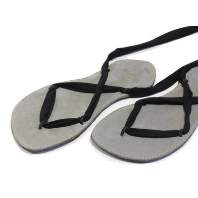A photo of Juuri ribbon sandals made from leather, viscose, and rubber soles. The sandals have a grey footbed and long black laces. Both sandals are shown up close beside each other from the front against a white background. #color_grey-black