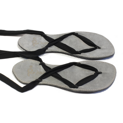 A photo of Juuri ribbon sandals made from leather, viscose, and rubber soles. The sandals have a grey footbed and long black laces. Both sandals are shown sitting beside each other facing to the right against a white background. #color_grey-black