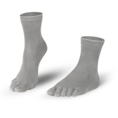 A photo of Knitido essential midi crew toe socks made with cotton, nylon, and elastane. The socks are a grey color. Both socks are shown beside each other angled slightly to the left, one of the socks heel is lifted off the floor against a white background. #color_grey