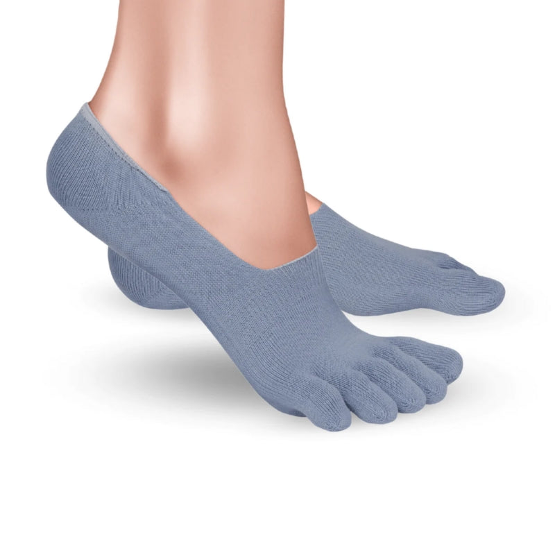 A photo of Knitido low cut toe socks made with cotton, nylon, polyester, and elastane. The socks are a blue/grey color. A woman is shown from ankle down wearing the low cut socks, she is facing to the right with right foot’s heel lifted slightly off the floor against a white background. #color_blue-grey
