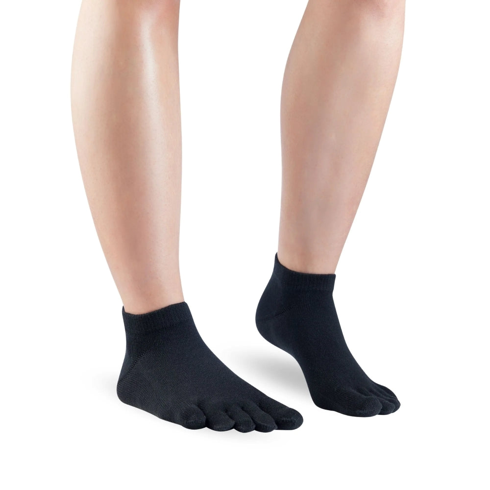 A pair of black Knitido ankle-height sneaker toe socks. Both socks are shown facing diagonally right against a white background on a person with the right heel up. #color_black