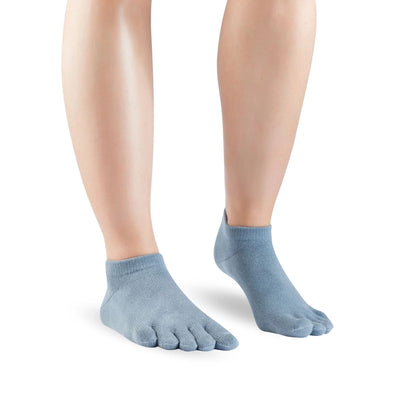 A pair of blue grey Knitido ankle-height sneaker toe socks. Both socks are shown facing diagonally right against a white background on a person with the right heel up. #color_blue-grey