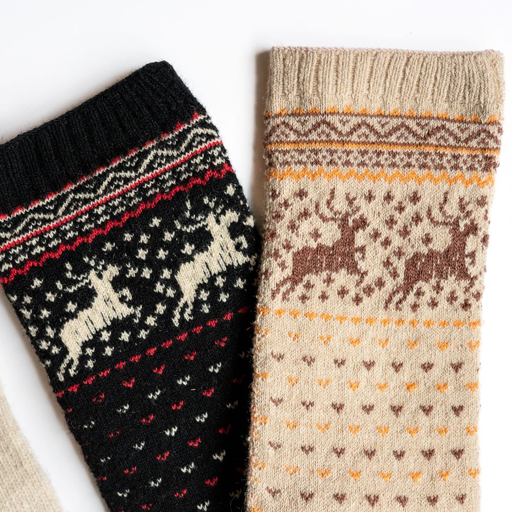 A photo of the Knitido Hossa reindeer sweater toe socks, which are cotton and wool blend. The socks are beige in color with brown and yellow festive details all over the sock and reindeer around the ankle. The ankle of the beige-brown Hossa socks and the black-beige Hossa socks are shown next to eachother, showing the reindeer details on a white background. #color_beige-brown