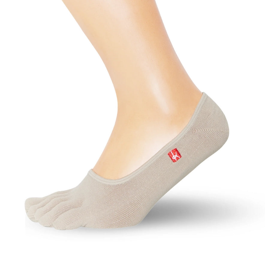 A photo of Knitido track and trail footies socks made with cotton, nylon, polyester, and elastane. The socks are a beige color. One sock is shown on a foot from mid leg down facing to the right side with it’s heel lifted slightly off the floor against a white background. #color_beige