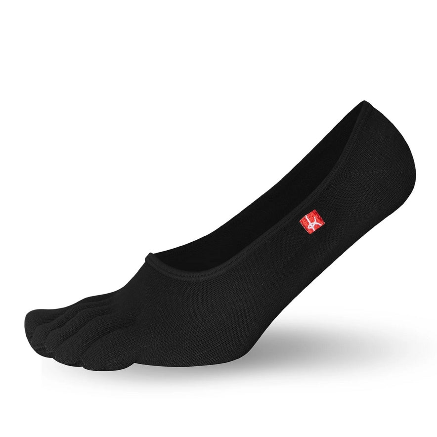 A photo of Knitido track and trail footies socks made with cotton, nylon, polyester, and elastane. The socks are a black color. One sock is shown facing to the left with the heel lifted slightly off the floor against a white background. #color_black