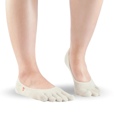 A pair of beige Knitido track and trail zero toe socks. Socks are very low cut to be invisible in shoes. Both socks are shown facing diagonally right against a white background on a person with the right heel up. #color_beige