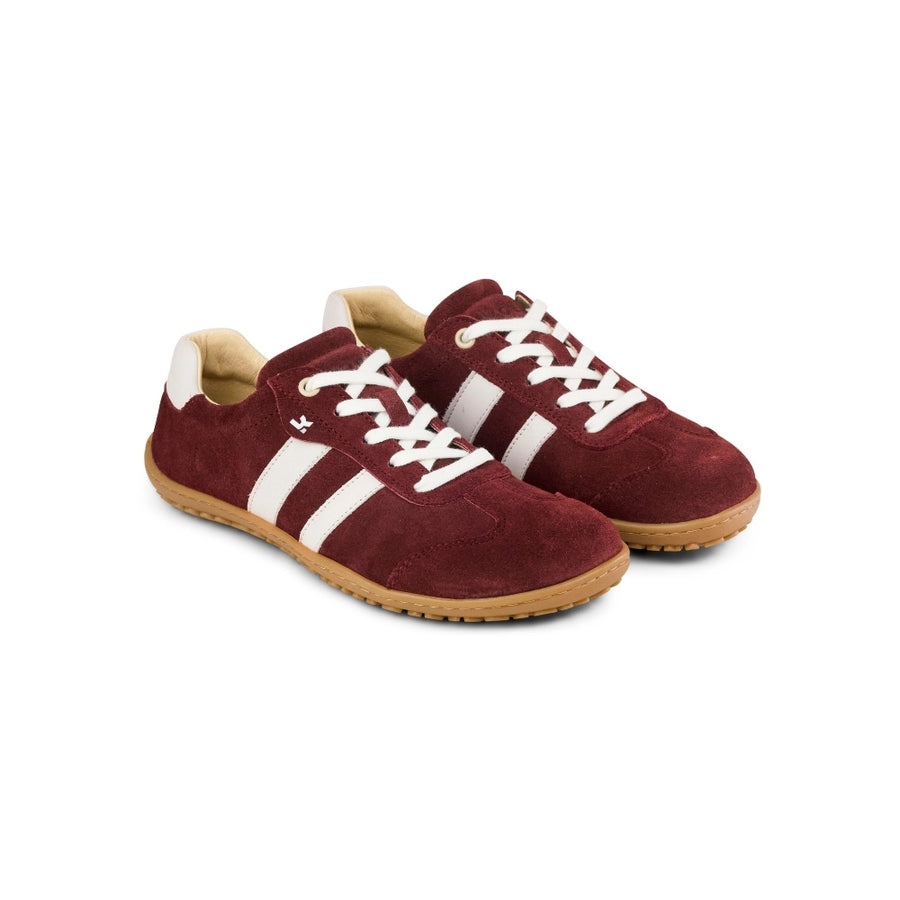 Suede deep red Koel Ila sneakers with two diagonal, white stripes on either side, white laces, and natural rubber soles. A suede Bordeaux T-shape design is present at the top of the toe box. Both shoes are shown facing diagonally right against a white background. #color_suede-bordeaux