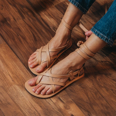 A close up side view of a woman's feet wearing Laboo x Anya leather barefoot sandals with adjustable straps in natural tan. #color_tan