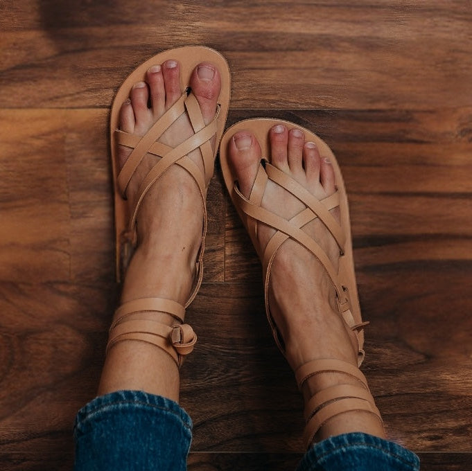 A top down view of a pair of woman's feet resting on a wood floor wearing Laboo x Anya barefoot leather sandals with adjustable straps and an ankle wrap in tan color. #color_tan