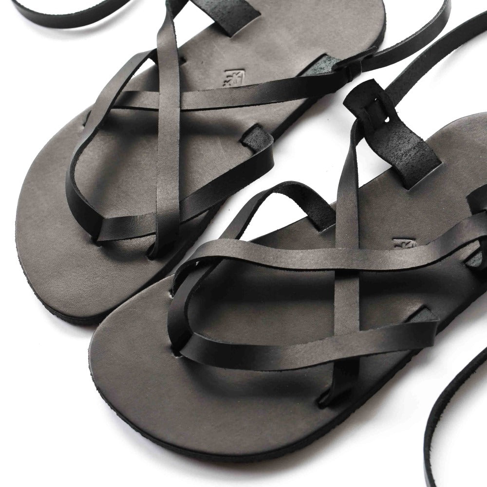 A black leather strappy sandal shown close up facing diagonally left on a white background. #color_black