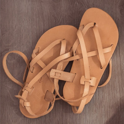 A light brown leather strappy sandal shown from above on a grey wooden floor. #color_tan