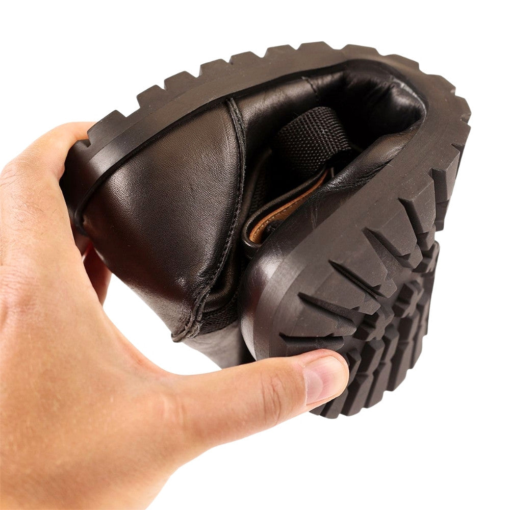 Black, smooth leather Lang.S Kombat boot, with round black laces, a pull tab, zipper, and chinky black soles. One shoe is shown in a hand rolled up to show flexibility against a white background. #color_black