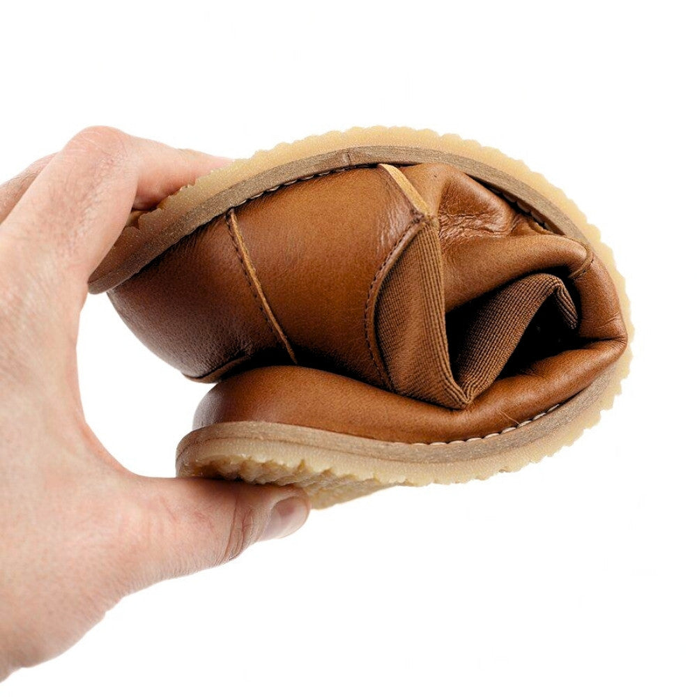 Brown leather Lang.S Luna Chelsea boots with a pull tab, tan interior leather, and tan rubber. One boot is shown folded in a left hand against a white background to show flexibility. #color_brown