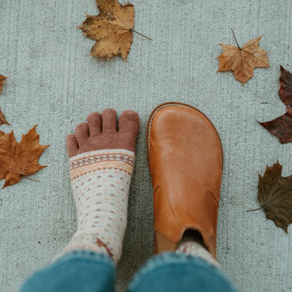 Brown leather Lang.S Luna Chelsea boots with a pull tab, tan interior leather, and tan rubber. Right boot is shown from above on a woman wearing medium wash, loose, cropped jeans, and tan reindeer patterned socks standing on cement. Left foot is only wearing a sock. #color_brown