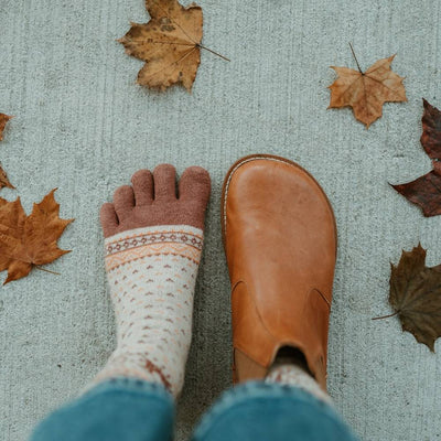 Brown leather Lang.S Luna Chelsea boots with a pull tab, tan interior leather, and tan rubber. Right boot is shown from above on a woman wearing medium wash, loose, cropped jeans, and tan reindeer patterned socks standing on cement. Left foot is only wearing a sock. #color_brown