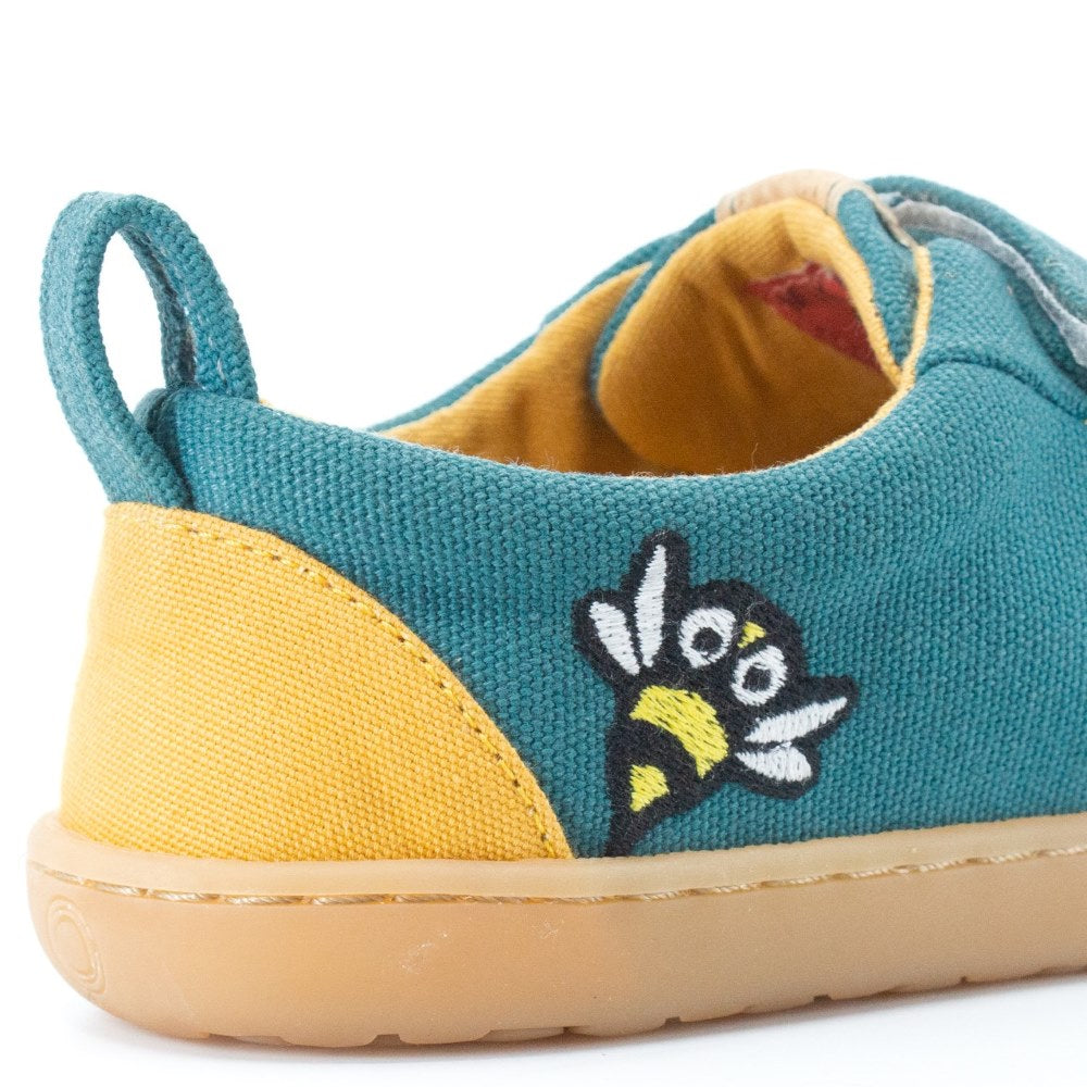 Abelha Dark Teal Mukishoes Play Kids shoe. Shoes are simple in design with velcro closures, an embroidered bee on the side close to the heel, a pull tab on the heel, a yellow color block on the heel, and yellow lining. Soles are a natural rubber gum color. Right shoe bee detail and heel is shown here against a white background. #color_abelha