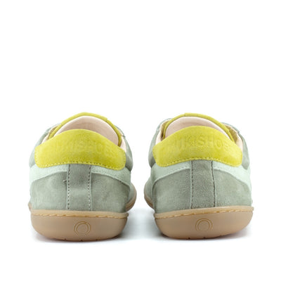 Theia (multiple green colors) Mukishoes Lyra suede leather sneakers with, white laces, and a natural rubber colored sole. Shoes are all sage green colored with a T-shaped detail on the toe box in sage green, a T-shaped seafoam green detail on both sides of the ankle, and neon green color detail on the top of the tongue and heel. Both shoes are shown from the back against a white background. #color_theia