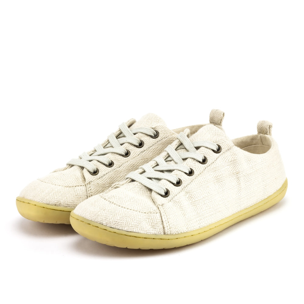 A photo of Mukishoes Sand fabric sneakers. Shoes are simple in design with a subtle herringbone pattern, brass-colored rivets, a pull tab on the back, and sand-colored lining, laces, and gum-colored soles. Both shoes are shown diagonally here facing slightly to the left against a white background. #color_sand