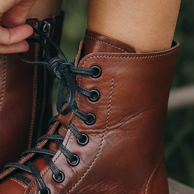 A photo of Peerko Go combat boots made with smooth leather, inside side zippers, and rubber soles. The boots are brown in color and fleece lined. A close up pf the left boot laces are shown here. #color_cognac