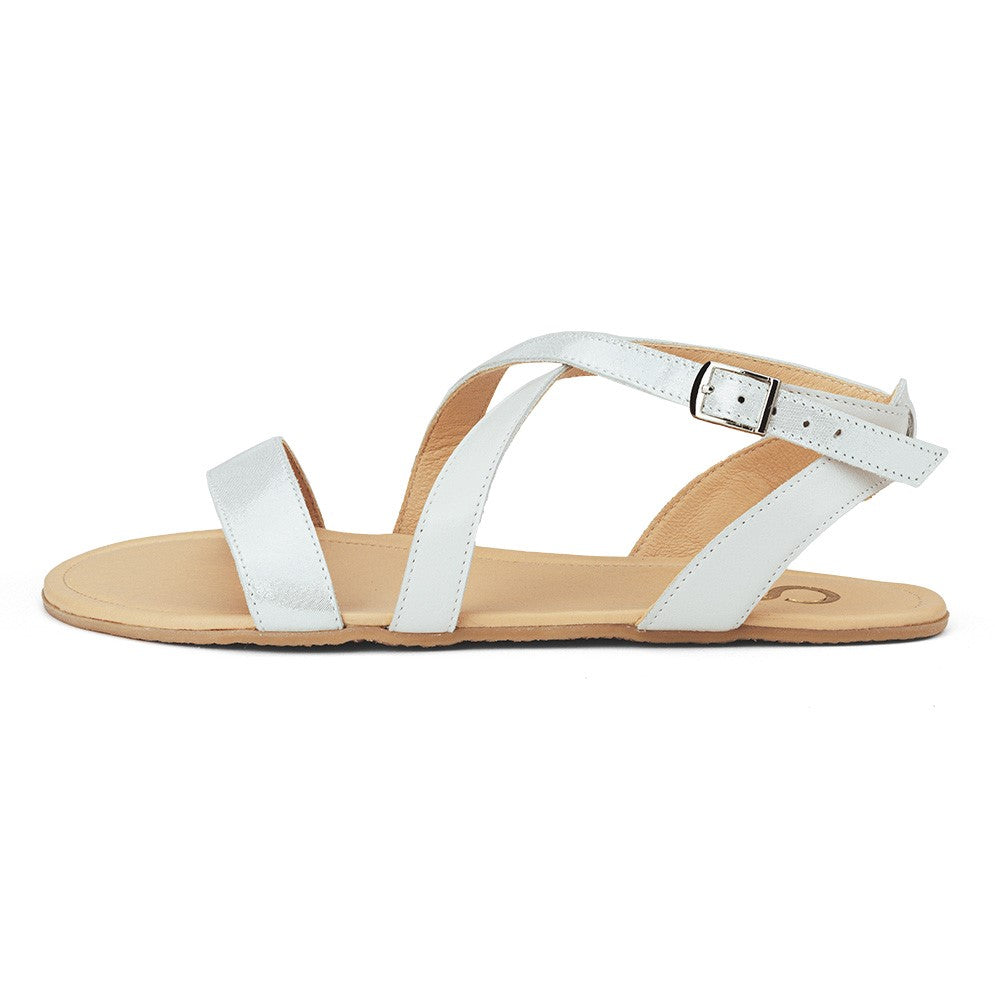 A photo of White Shapen Calla Sandals made with leather and tan rubber soles. The sandals have a slight sparkle. Left sandal is shown from the left side against a white background in this photo. #color_white