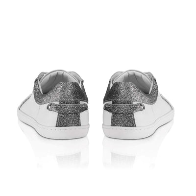 A photo of Shapen Feelin Chic leather sneakers in white. Sneakers have dark grey glitter blocks around the foot opening and a scalopped glitter detail enhancing both sides of the laces. Glitter detail also goes down the back with a glitter pull tab attached by rivets. Both shoes are shown from the back here against a white background. #color_white-glitter