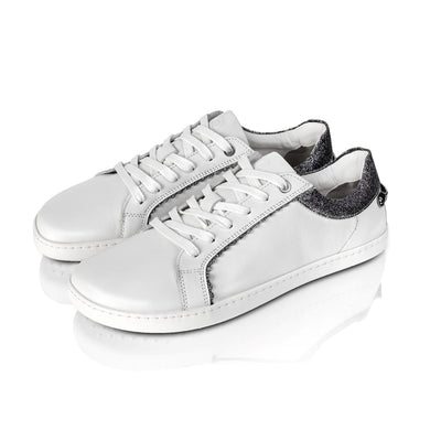 A photo of Shapen Feelin Chic leather sneakers in white. Sneakers have dark grey glitter blocks around the foot opening and a scalopped glitter detail enhancing both sides of the laces. Both shoes are shown here diagonally from the front left against a white background. #color_white-glitter