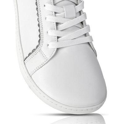 A photo of Shapen Feelin Chic leather sneakers in white. Sneakers have dark grey glitter blocks around the foot opening and a scalopped glitter detail enhancing both sides of the laces. Right shoe toe box is shown here against a white background. #color_white-glitter