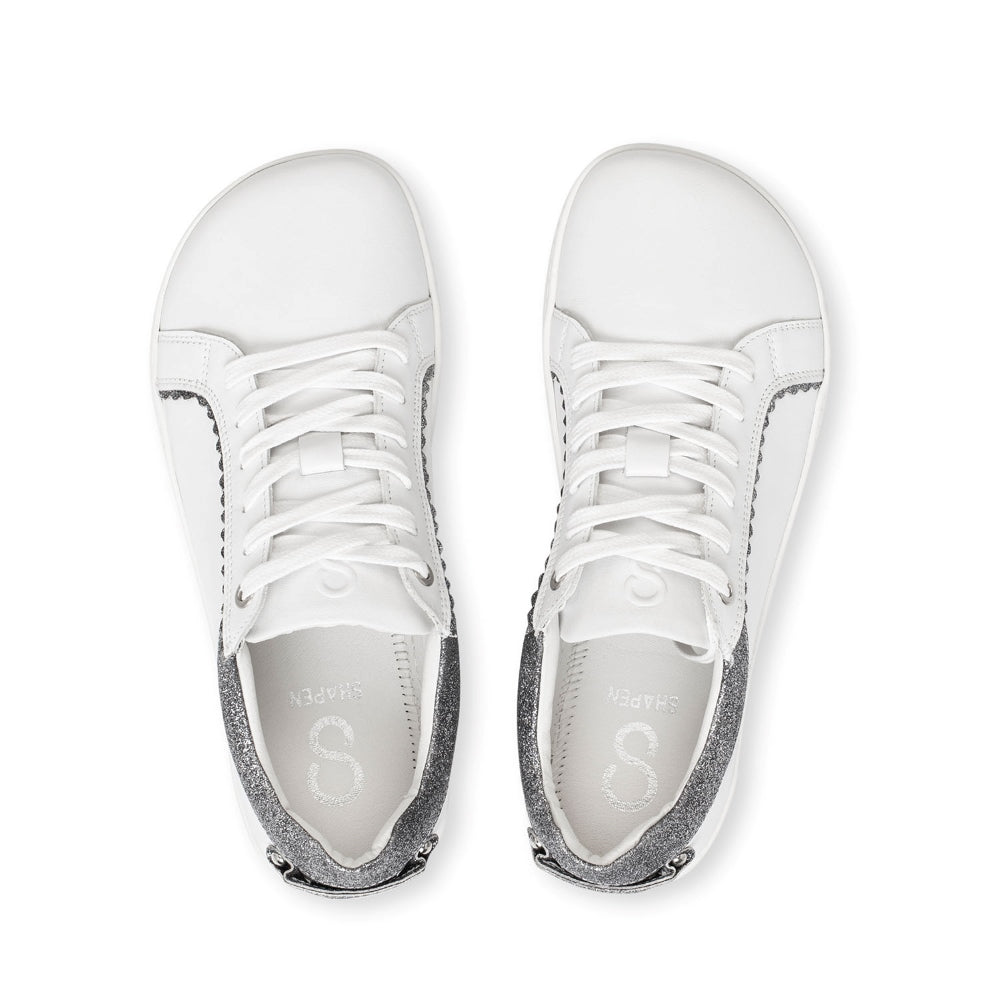 A photo of Shapen Feelin Chic leather sneakers in white. Sneakers have dark grey glitter blocks around the foot opening and a scalopped glitter detail enhancing both sides of the laces. Both shoes are shown here from the top down against a white background. #color_white-glitter