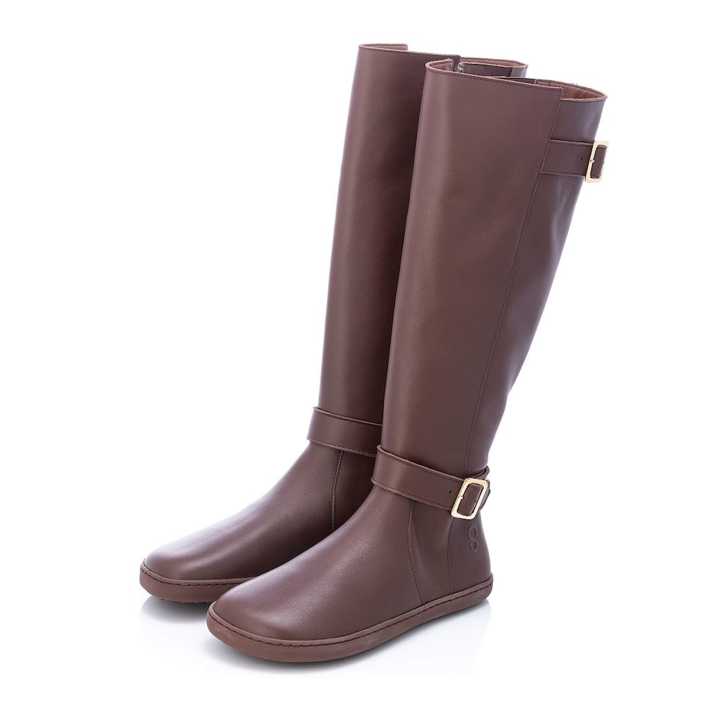 A photo of Shapen Glam lined riding boots made with leather, a faux fur lining, and brown rubber soles. The boots are brown in color with gold buckles on the top and around the ankle, the ankle buckle strap is removable. Both boots are shown facing diagonally left against a white background. #color_brown