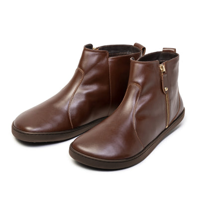 A photo of Shapen Ivy Chelsea boots made from smooth leather and rubber soles. The boots are brown in color with stitching detailing and have a gold zipper with a leather tab on the side. Both boots are shown beside each other facing forward angled slightly to the right side against a white background. #color_brown