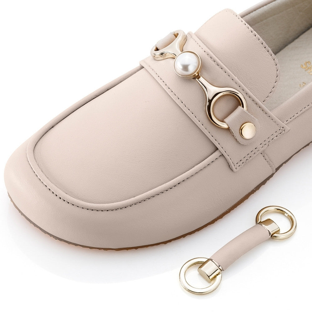 A gold metal accessory for the Shapen Versa Loafer. Chain is attached by a D shape on either side that tapers into holding a pearl detail in the middle. Accessory is shown on a beige Shapen Versa loafer facing diagonally left against a white background next to the normal leather accessory sitting next to the shoe. #color_gold-pearl