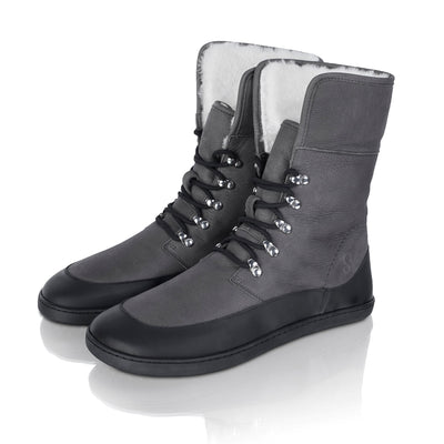 A photo of the Shapen Lynx lace up boots made from a water-resistant nubuck leather uppers and black rubber soles. The boots are dark grey in color, have a black leather rim around the bottom inch of the shoe, black laces, and a white wool lining that can be shown by folding over the top of the boots. Both boots are shown together from the front left side on a white background. #color_dark-grey
