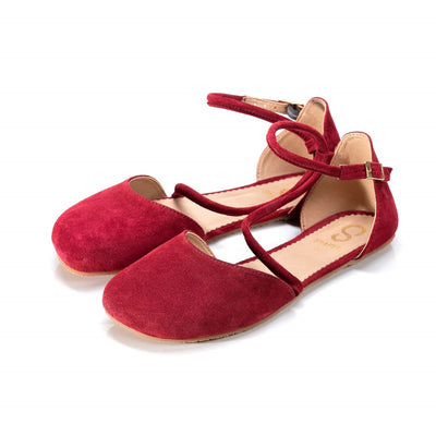 A photo of dark red Shapen Orchid flats.  Shoes are suede with tan rubber soles. A toe box and heel cup bookmark each end of the shoe with a round strap that zig zags from the toe box to the ankle/heel cup to keep the shoes secured to the foot. Both shoes are shown pointed slightly left here against a white background. #color_bordeaux