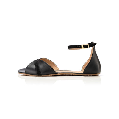 Black Shapen Petal Sandals. Sandals are a peep toe style at the toe box and a heel cup attached to a thin, suede ankle strap. Left shoe is shown here facing left against a white background. #color_black