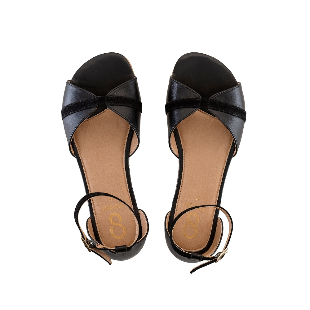 Black Shapen Petal Sandals. Sandals are a peep toe style at the toe box and a heel cup attached to a thin, suede ankle strap. Both shoes are shown from above here against a white background. #color_black