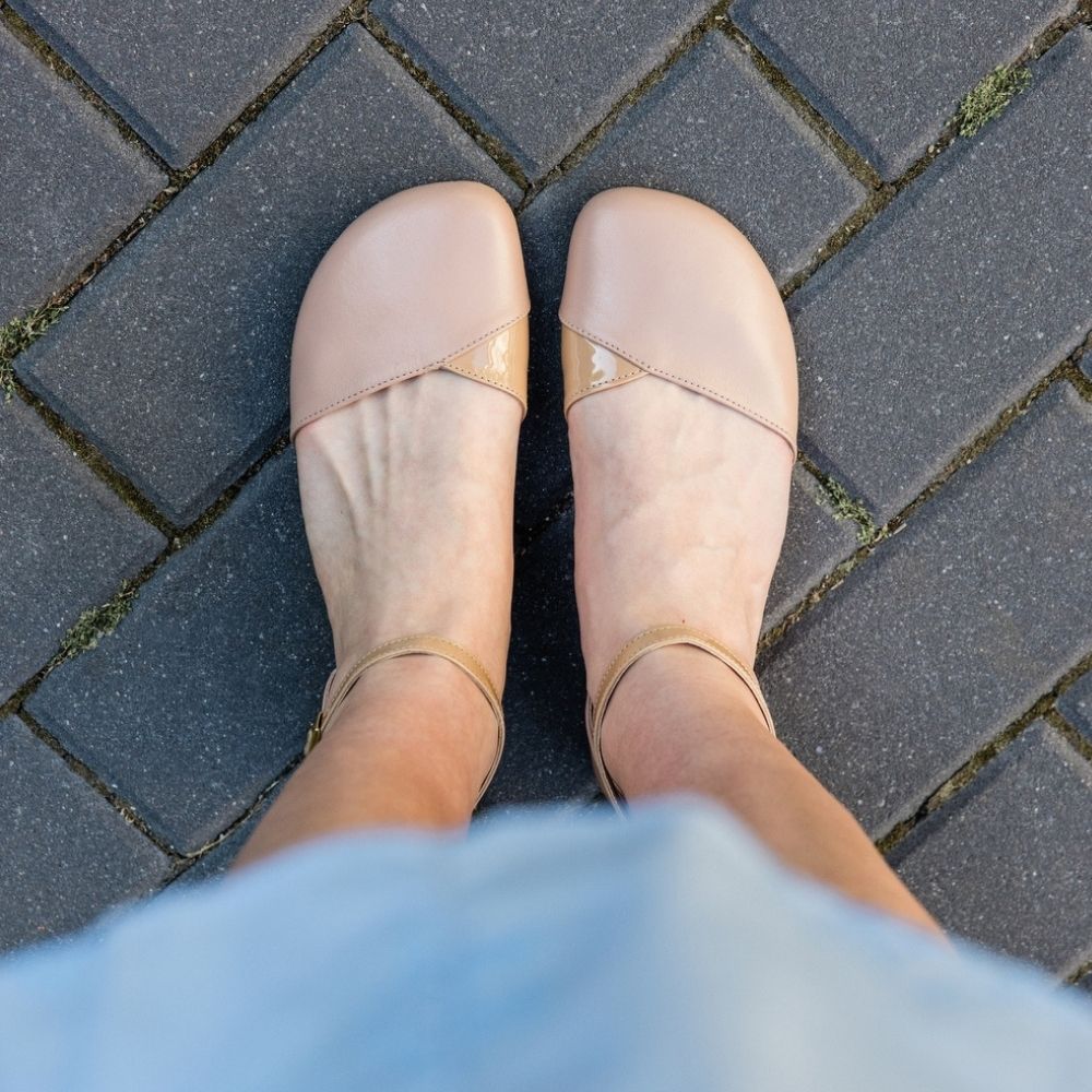 Beige, leather Shapen Poppy D’orsay dressy flats with tan rubber soles. The flats have a heel cup and dainty ankle straps. Both shoes are shown from above on a light-skinned woman standing on a grey brick pathway. #color_beige 