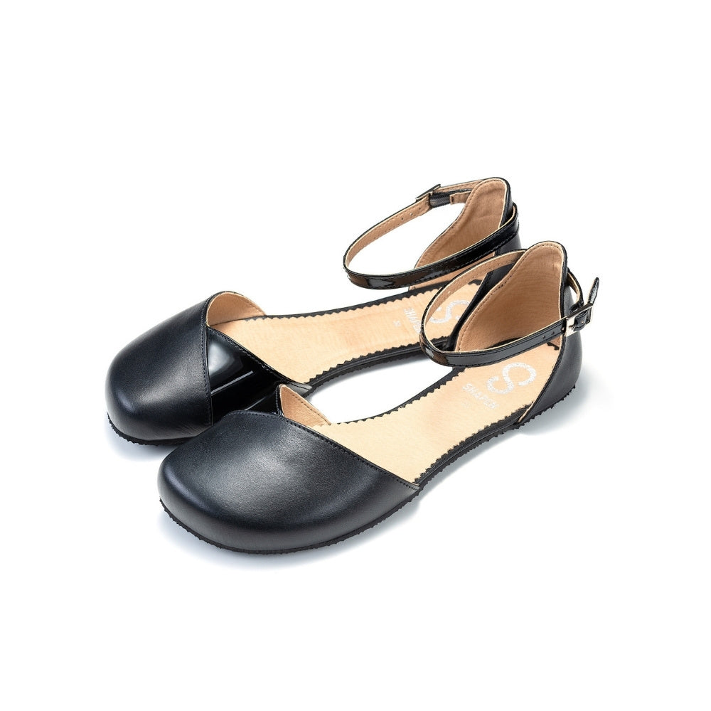 Black leather Shapen Poppy D’orsay dressy flats with a tan footbed and tan rubber soles. The flats have a heel cup held on by a dainty, patent leather ankle strap. Both flats are shown facing diagonally left against a white background. #color_black