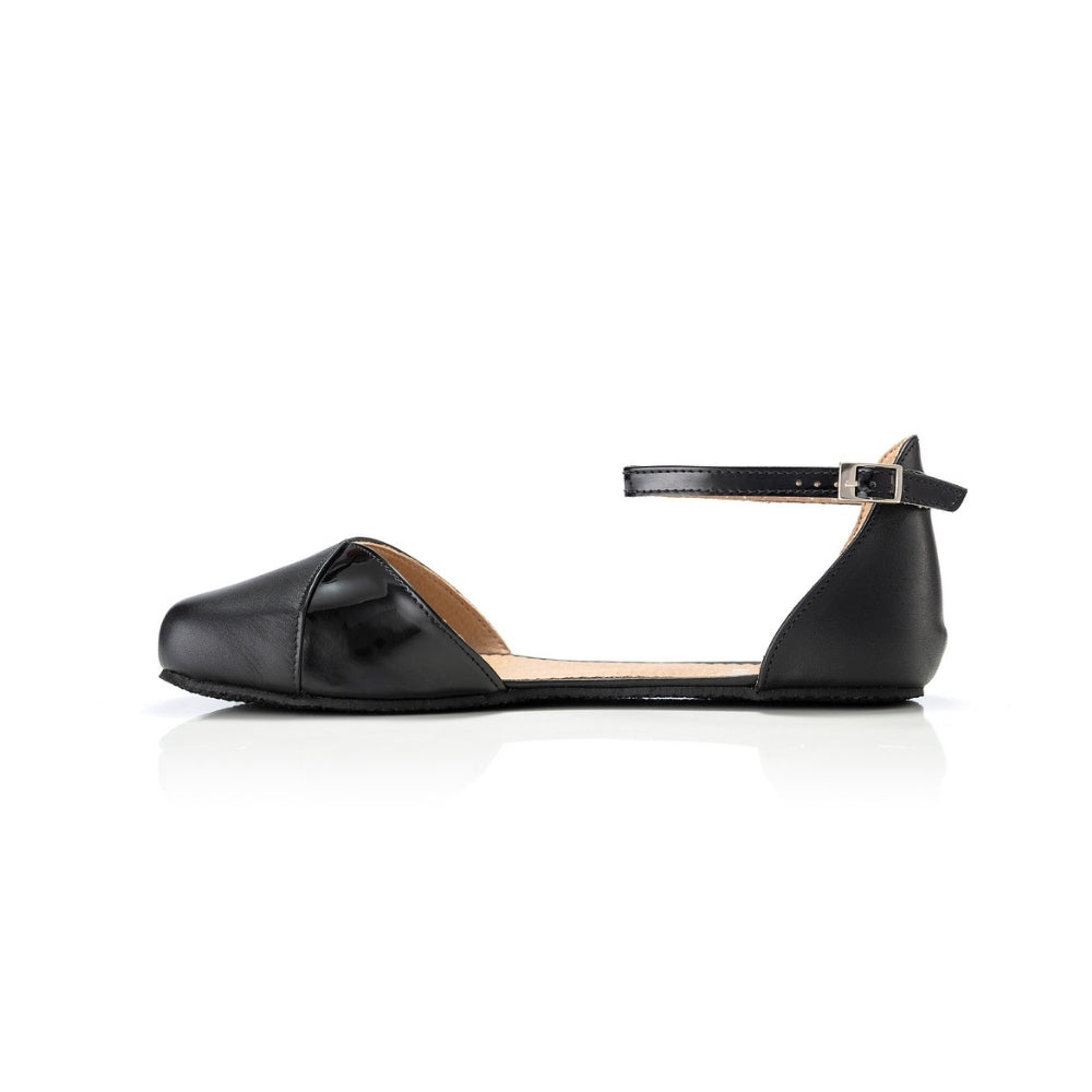 Black leather Shapen Poppy D’orsay dressy flats with a an footbed and tan rubber soles. The flats have a heel cup held on by a dainty , patent leather ankle strap. Right flat is shown facing left against a white background. #color_black