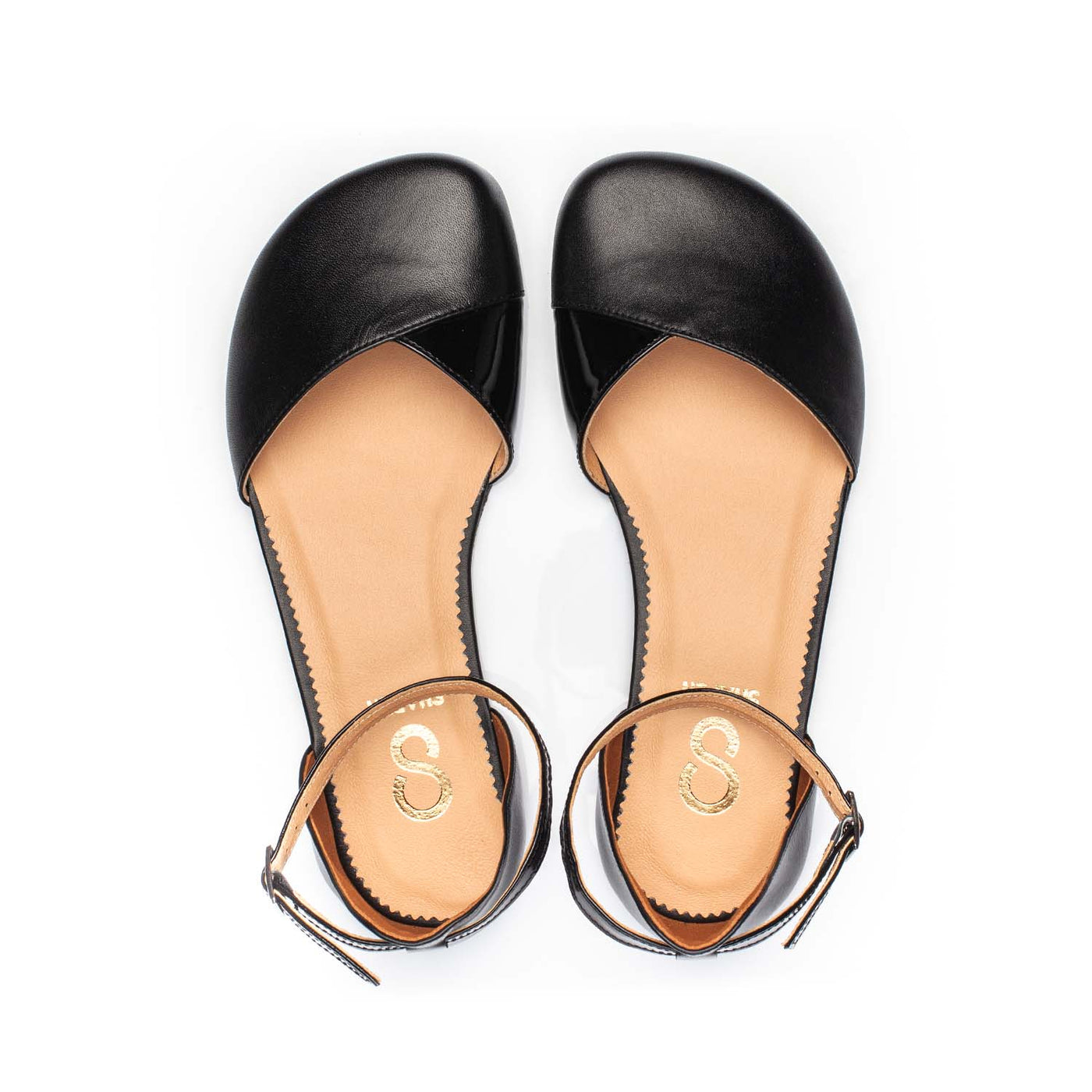 A photo of Shapen Poppy D’orsay dressy flats with a leather upper and rubber soles. The flats are a black color with a heel cup and dainty ankle strap, the inside of the sole are a beige color. Both flats are shown from the top facing up against a white background. #color_black