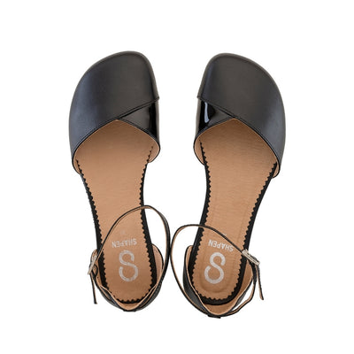 Black leather Shapen Poppy D’orsay dressy flats with a tan footbed and tan rubber soles. The flats have a heel cup held on by a dainty, patent leather ankle strap. Both flats are shown from above against a white background. #color_black