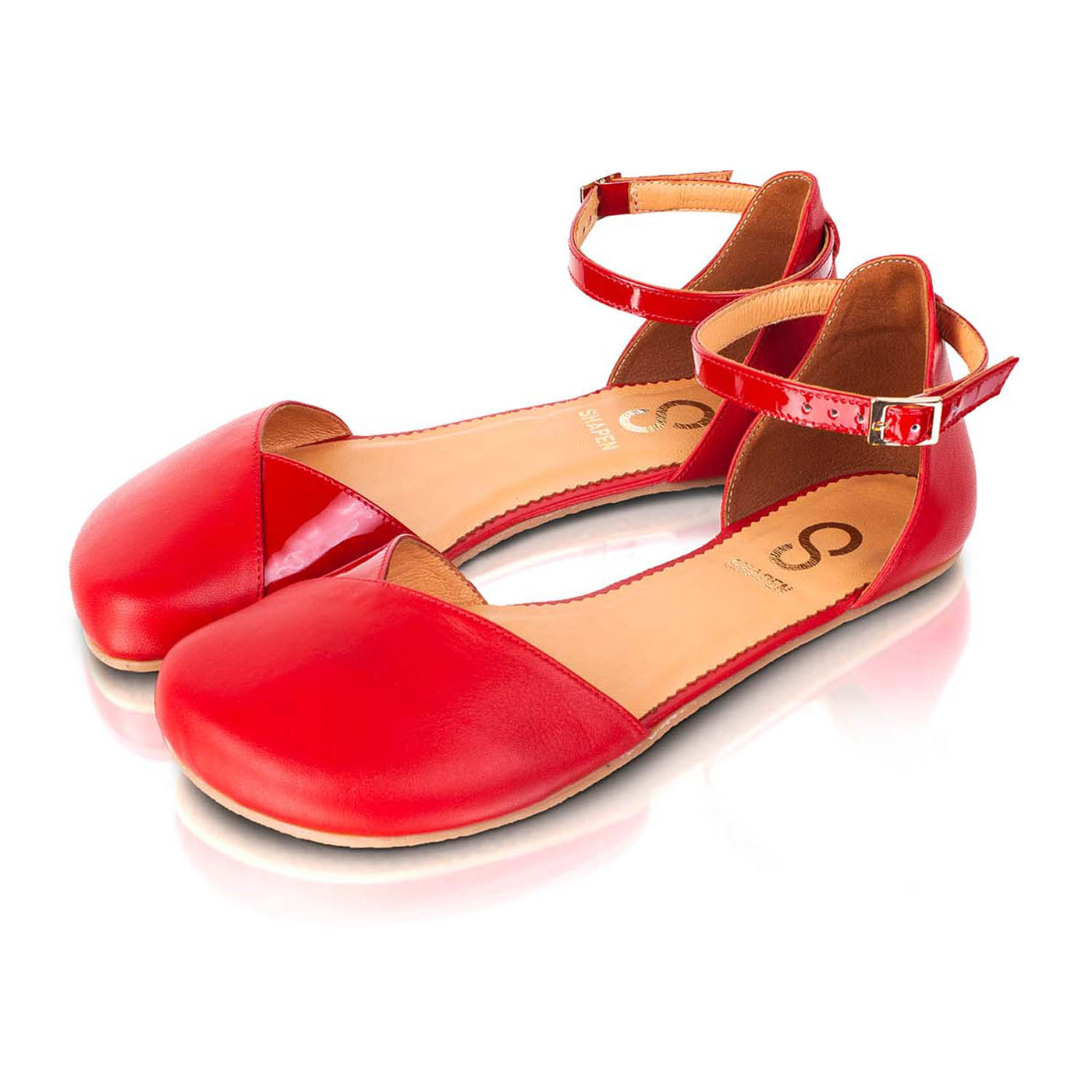 A photo of Shapen Poppy D’orsay dressy flats with a leather upper and rubber soles. The flats are a cherry red color with a heel cup and dainty ankle strap, the inside of the sole are a beige color. Both flats are shown beside each other turned with the right shoe towards the front against a white background. #color_red