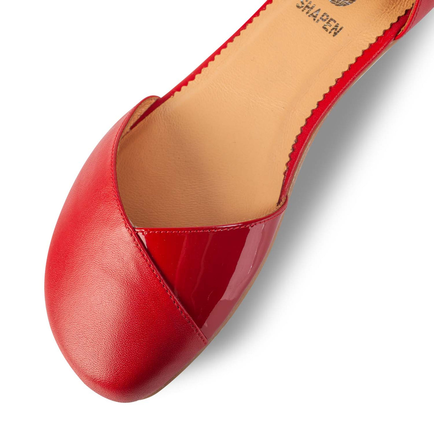 A photo of Shapen Poppy D’orsay dressy flats with a leather upper and rubber soles. The flats are a cherry red color with a heel cup and dainty ankle strap, the inside of the sole are a beige color. The right shoe is shown up close from the front against a white background. #color_red