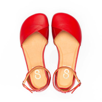 A photo of Shapen Poppy D’orsay dressy flats with a leather upper and rubber soles. The flats are a cherry red color with a heel cup and dainty ankle strap, the inside of the sole are a beige color. Both flats are shown from the top facing up against a white background. #color_red